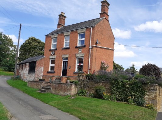 Brick Victorian house with workshop attached.  Detailed chimneys sit at either gable end of the two-storey house.