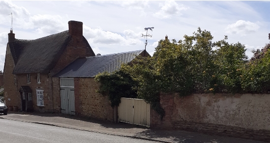 Image of High Street showing stone and thatched former Post Office, outbuilding with double gates and double garden gates adjacent to stretch of mud wall.