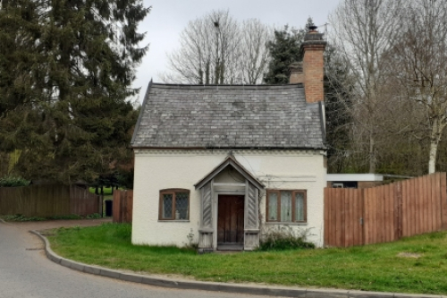 Small, single storey, white cottage with pitched slate roof and two chimneys.  Central door with windows either side